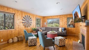 A wooden-paneled room with a sectional sofa, two armchairs, a round coffee table, and a fireplace.