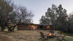 A house with a fire pit and chairs in the yard.