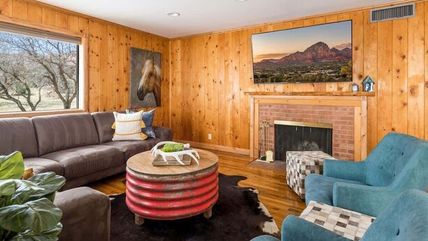 A cozy living room with a wooden interior, a fireplace, a large window, and a mounted painting.