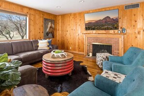 Un salón acogedor con interior de madera, una chimenea, un ventanal grande y un cuadro colgado.