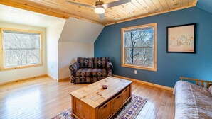 A room with a sloped ceiling, wooden floors, a patterned sofa, a wooden coffee table, and large windows with a view of bare trees. - Hot Tub in 39 Acres of Aspens - Mtn Views, 23mi to Breck, Pet-Friendly (Fairplay)