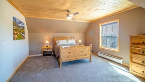 A bedroom with a wooden ceiling, a bed, a nightstand, a dresser, and a window. - Hot Tub in 39 Acres of Aspens - Mtn Views, 23mi to Breck, Pet-Friendly (Fairplay)