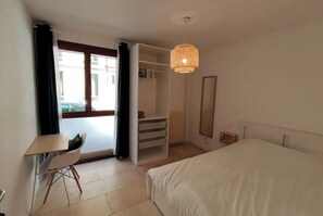 A hotel room with a bed, a desk with a chair, a wardrobe, and a hanging light fixture.