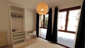 Ein Zimmer mit einem Bett, einem Schreibtisch, einem Kleiderschrank und einem großen Fenster mit Vorhängen.