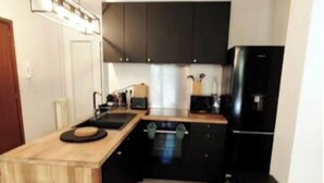 Eine kleine Küche mit dunklen Schränken, einem schwarzen Kühlschrank und einer Holz Arbeitsplatte.