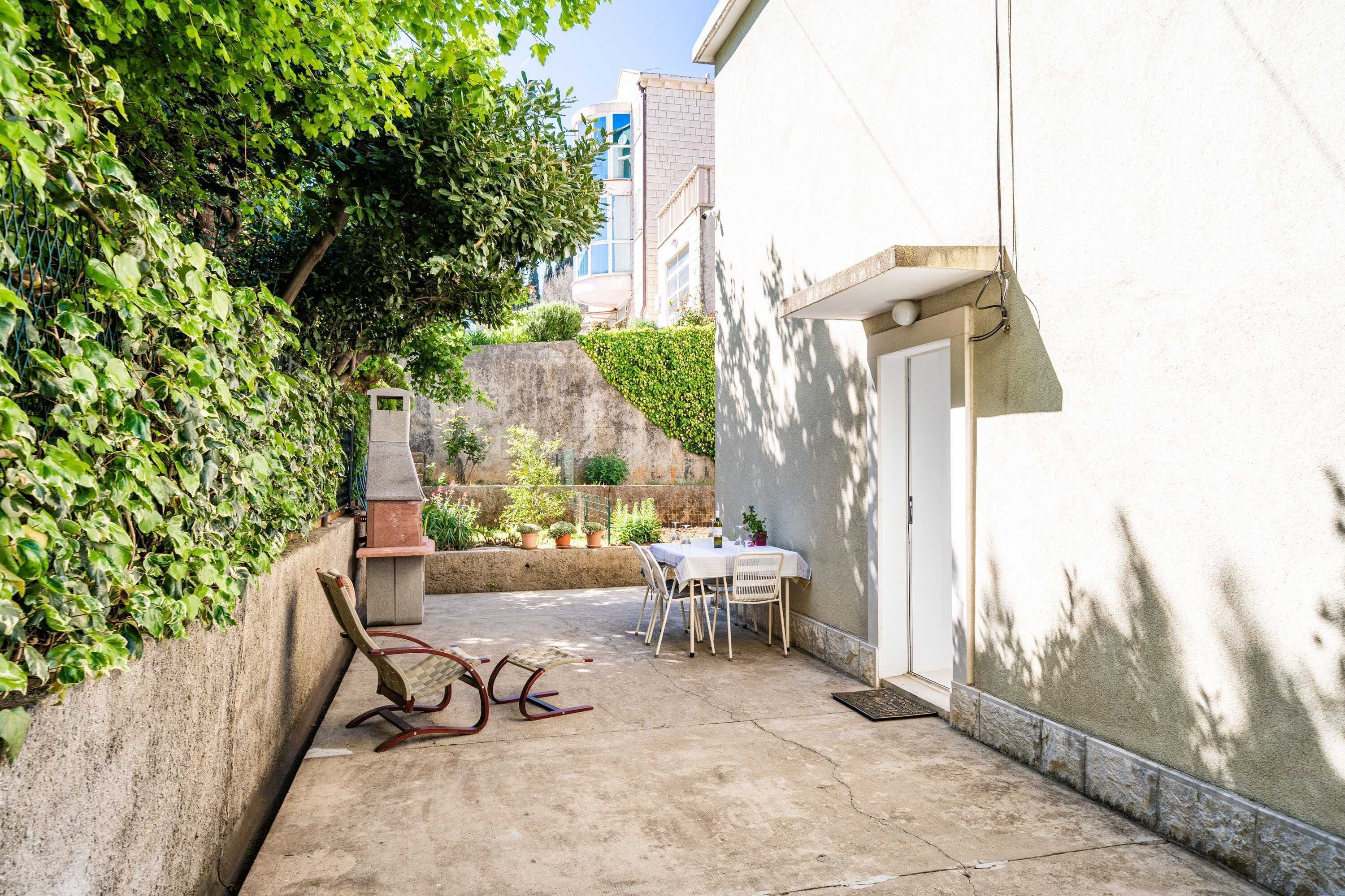 Un patio con mesa y sillas, una parrilla y una pared cubierta de plantas trepadoras.