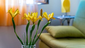A clear view of a vase with yellow flowers on a table in a room with a sofa and a lamp in the background. - Apartment Kos (Dubrovnik)