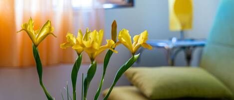 Se ve claramente un jarrón con flores amarillas sobre una mesa en una habitación con un sofá y una lámpara al fondo.