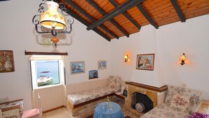 A cozy room with a wooden ceiling, a fireplace, floral-patterned sofas, a dining table, and a window with a view of the sea. - THE COTTAGE (Nisaki)
