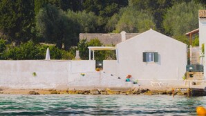 A coastal building with a white exterior, a small window, and a door. There is a white wall with a small balcony and a potted plant. - THE COTTAGE (Nisaki)