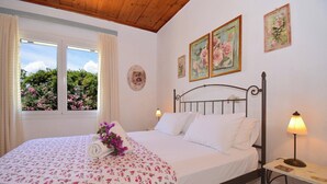 A bedroom with a bed, two bedside lamps, a window with curtains, and floral artwork on the walls. - THE COTTAGE (Nisaki)