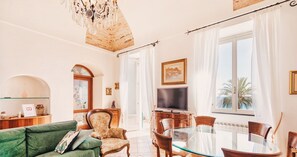A spacious living area with a green sofa, a glass dining table, and a TV.