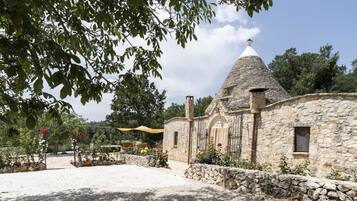 Un bâtiment en pierre surmonté d’un toit conique, entouré d’une zone recouverte de gravier et de murs en pierre.