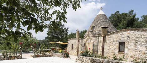 A stone building with a conical roof, surrounded by a gravel area and stone walls.