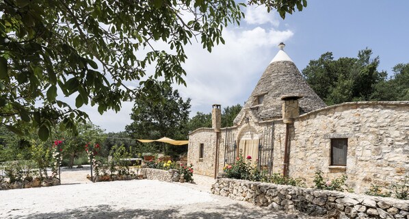 A stone building with a conical roof, surrounded by a gravel area and stone walls.