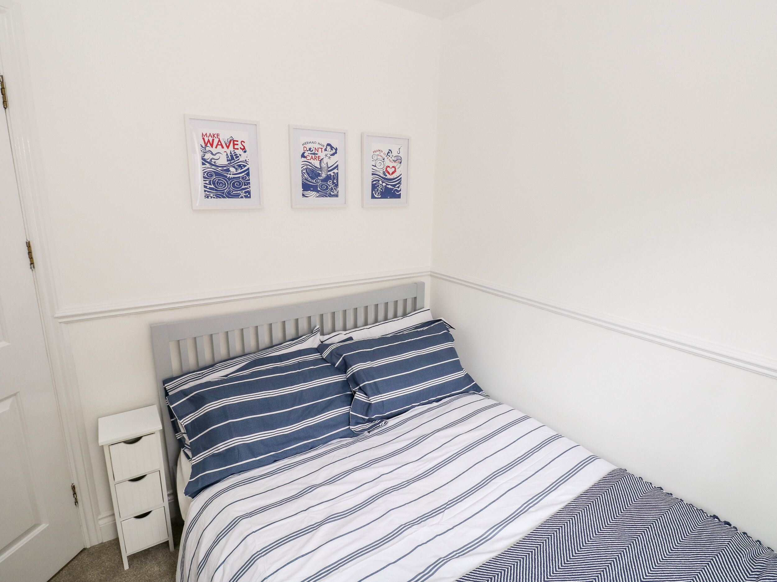 A bedroom with a bed, a nightstand, and three framed posters on the wall.