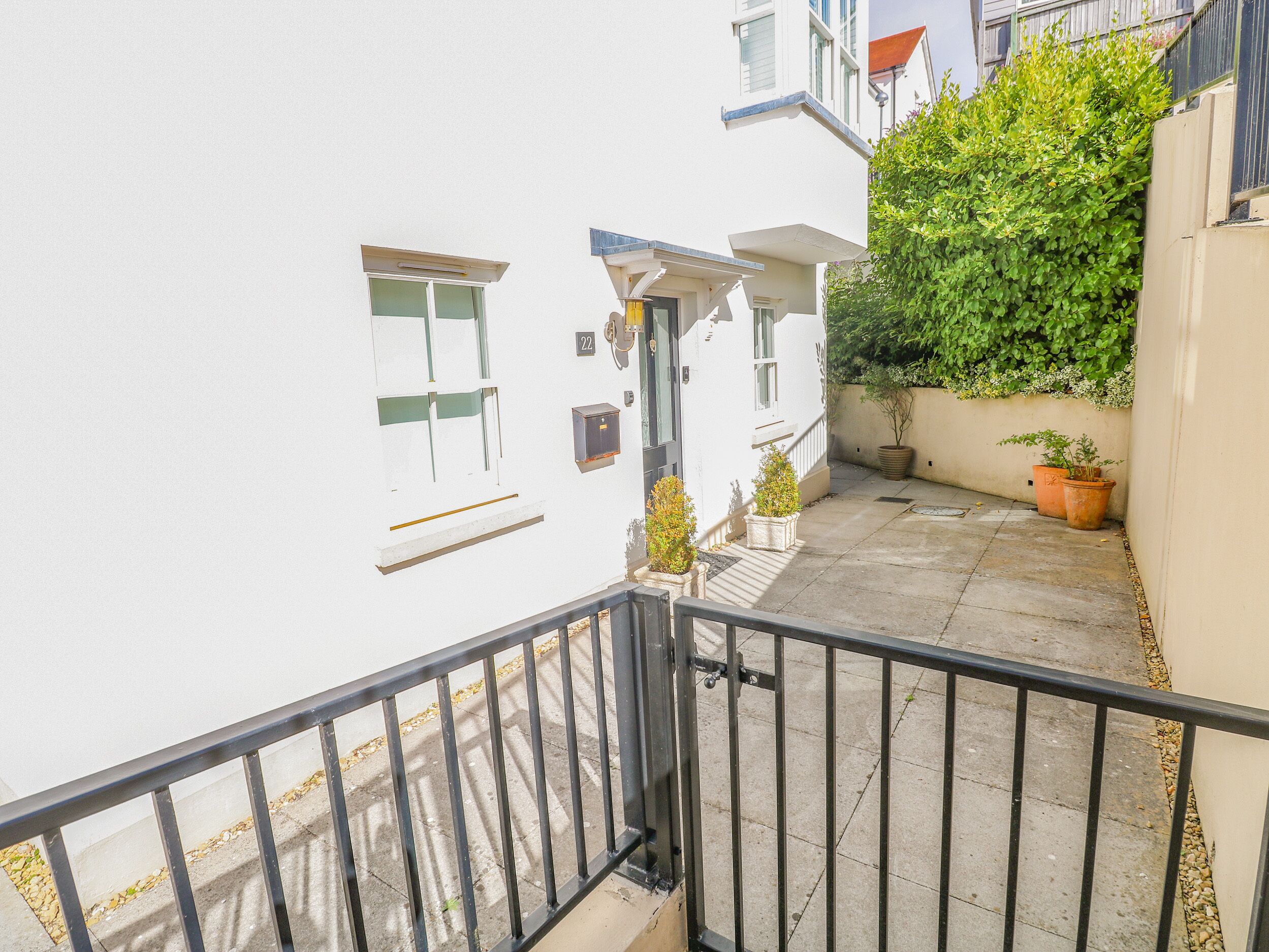 A narrow outdoor corridor with a white building, a metal railing, and potted plants.