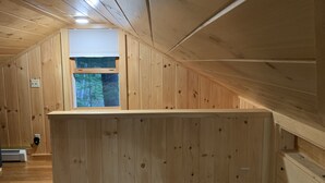 En träinredd interiör med ett sluttande tak, ett fönster med utsikt över träd och en inbyggd bänk.