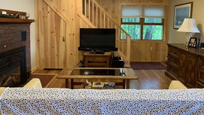 Ett mysigt vardagsrum med träinredning, en öppen spis, en tv och en trappa som leder upp till ett annat plan.