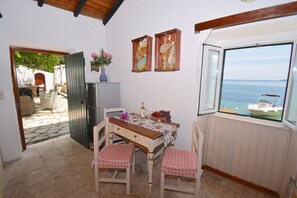A dining area with a table set for four, a refrigerator, and a window with a view of the sea.