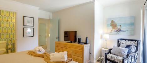 A hotel room with a bed, a wooden dresser, a chair, a television, and artwork on the walls.
