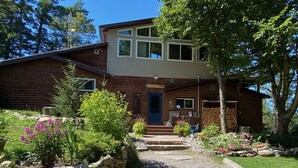 A two-story log cabin with a stone wall and gravel driveway leading to a blue door. - Beautiful Mink Lake, Close to Algonquin Park (Lake St. Peter)