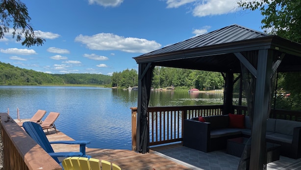 A wooden deck with Adirondack chairs, a covered seating area, and a view of a lake. - Beautiful Mink Lake, Close to Algonquin Park (Lake St. Peter)