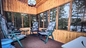 A wooden-paneled room with large windows, a hanging light fixture, and three chairs with floral upholstery. - Beautiful Mink Lake, Close to Algonquin Park (Lake St. Peter)
