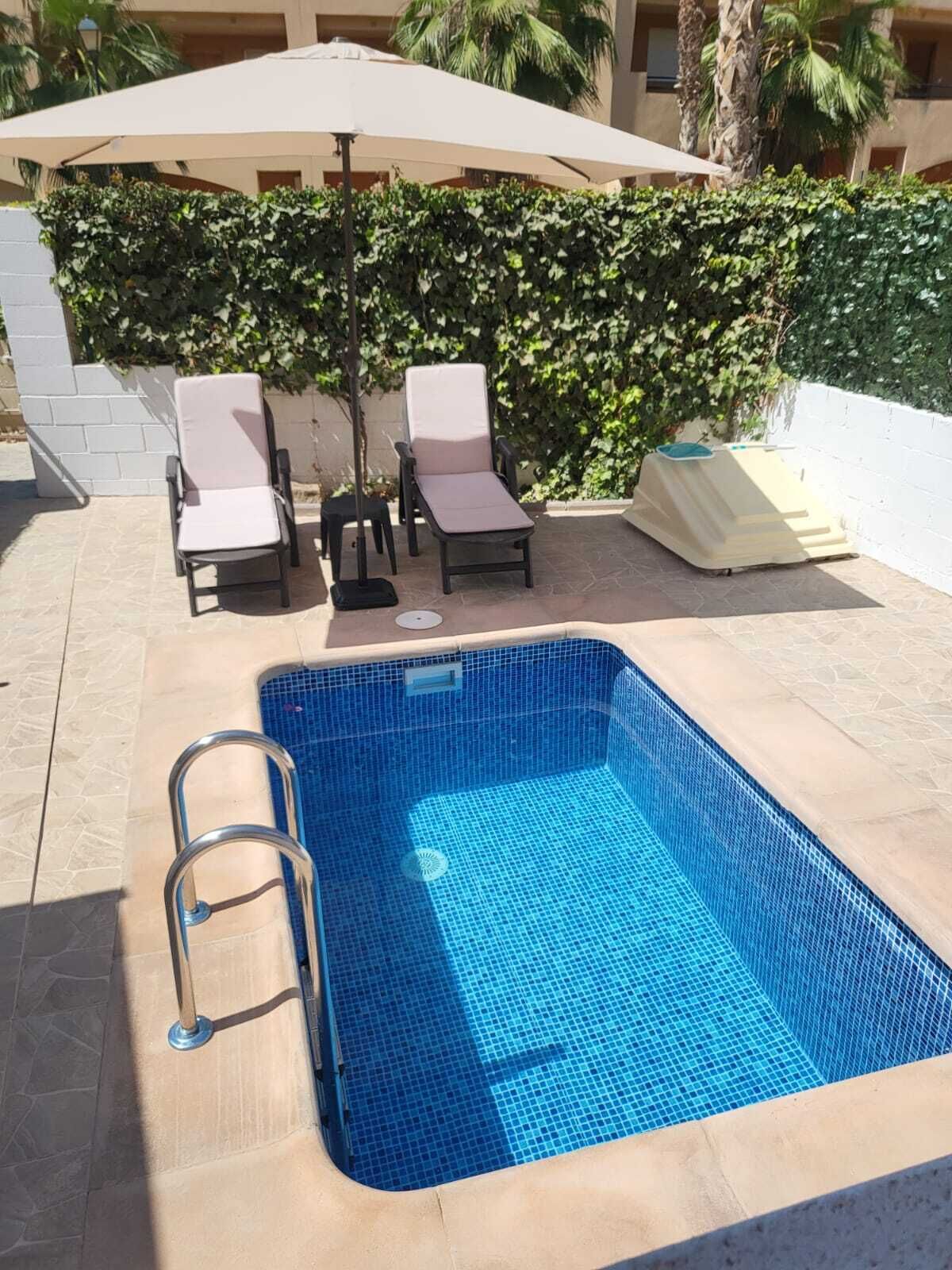 A rectangular swimming pool with a tiled blue interior, surrounded by lounge chairs and a sun umbrella.