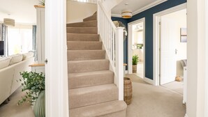 A staircase with beige carpet leading to a landing, white railings, and a basket on the floor. - Coral House (Cromer)
