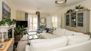 A living room with a sofa, a television, a cabinet with glass doors, and a dining area with a table and chairs. - Coral House (Cromer)