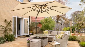 An outdoor patio area with a wicker sofa, ottomans, a glass table, and a lantern. - Coral House (Cromer)