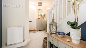 A hallway with a white radiator, a wooden console table with a bowl and a potted plant, and a staircase with white railings. - Coral House (Cromer)