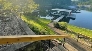 Eine Treppe führt zu einem Steg mit Booten, umgeben von viel Grün und einem klaren Himmel.