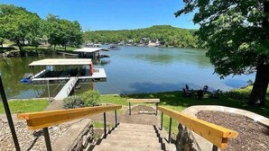 Blick auf einen See mit anlegenden Booten, eine Anlegestelle mit überdachtem Bereich und eine Treppe, die zum Wasser führt.