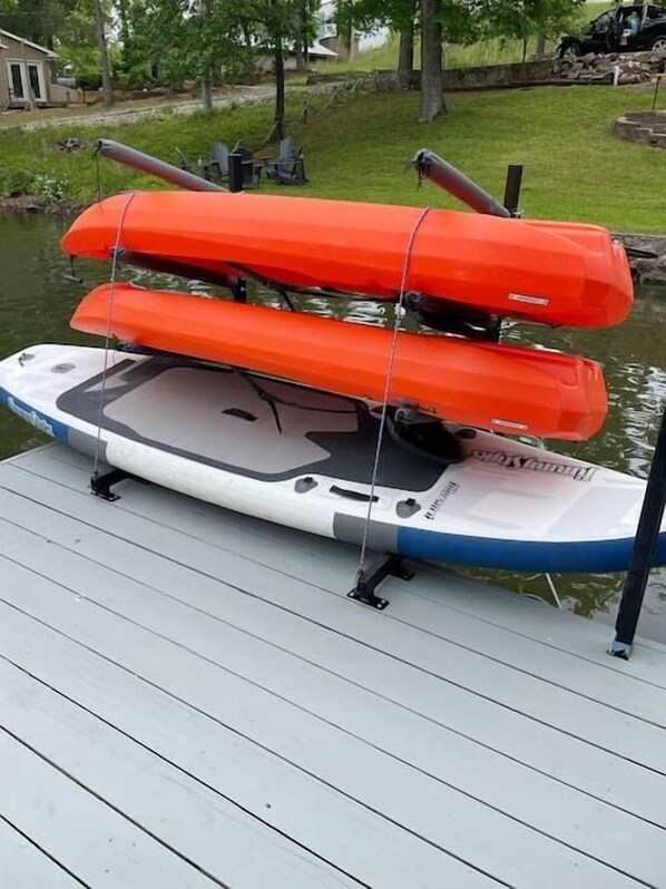 A white and blue paddleboard with two orange paddles secured on top, docked at a wooden pier.