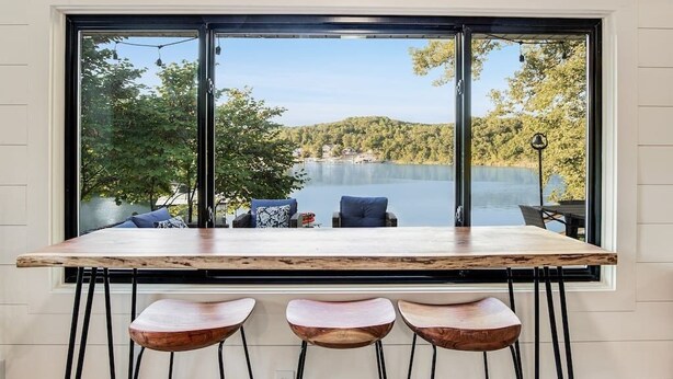 Ein Essbereich mit großem Fenster und Seeblick, einem Holztisch und drei Barhocker.