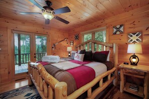 A wooden cabin bedroom with a bed, a ceiling fan, and a nightstand with a lamp.