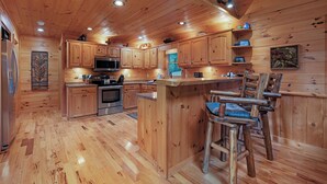 Interieur van een houten blokhut met een keuken, inclusief houten kastjes, een magnetron en een bar met krukken.