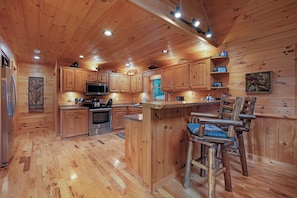 A wooden cabin interior with a kitchen featuring wooden cabinets, a microwave, and a bar area with stools. - Soaring Hawk Lodge - Morganton, GA (Morganton)