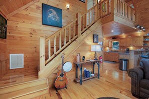 A wooden interior with a staircase, a guitar, a table with items, and a couch.
