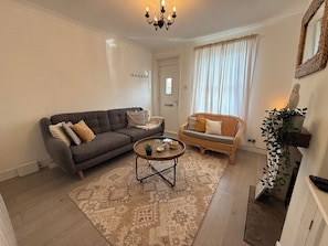 A living room with a grey sofa, a wicker chair, a coffee table, and a patterned rug. - Coastal Cottage at Sea Palling dog friendly (Sea Palling)