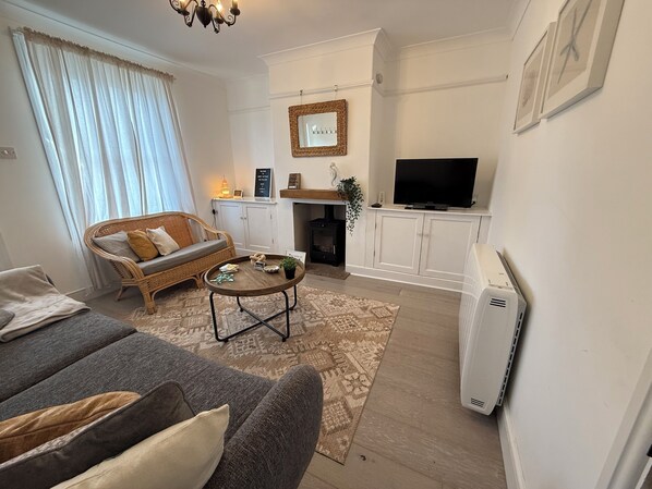 A living room with a sofa, a coffee table, a fireplace, a television, and a white cabinet. - Coastal Cottage at Sea Palling dog friendly (Sea Palling)