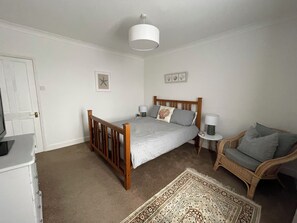 A bedroom with a bed, bedside tables, a chair, a rug, and a door. - Coastal  Cottage at Sea Palling dog friendly (Sea Palling)