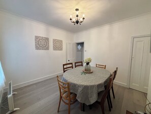 A dining room with a round table, wooden chairs, a chandelier, and two wall-mounted decorative pieces. - Coastal  Cottage at Sea Palling dog friendly (Sea Palling)