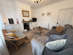 A cozy living room with a sofa, a wicker chair, a television, and a fireplace. - Coastal  Cottage at Sea Palling dog friendly (Sea Palling)