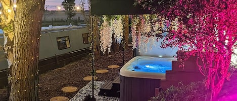 A hot tub area with a tree and hanging lights, surrounded by a garden with stepping stones.