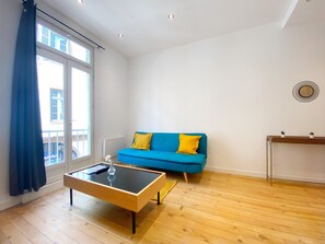En moderne stue med en blå sofa, et glasbord og trægulv.
