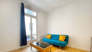 Una sala de estar moderna con un sofá azul, suelo de madera y una mesa de centro de cristal.