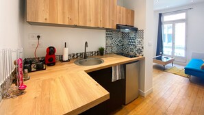 Una cocina moderna con armarios de madera, un lavamanos de acero inoxidable y una pequeña isla. Hay un hervidor rojo y un rollo de toallas de papel en la encimera.